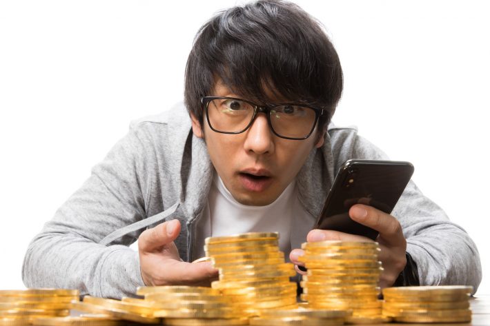 スマートフォンでトレードしている男性と金貨